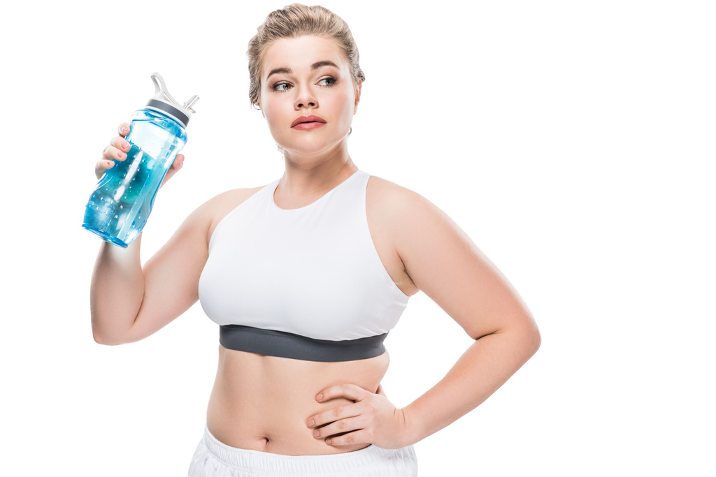 Größe plus Frau in Sportkleidung, die eine Flasche Wasser in der Hand hält und isoliert auf weiß wegschaut - Foto, Bild