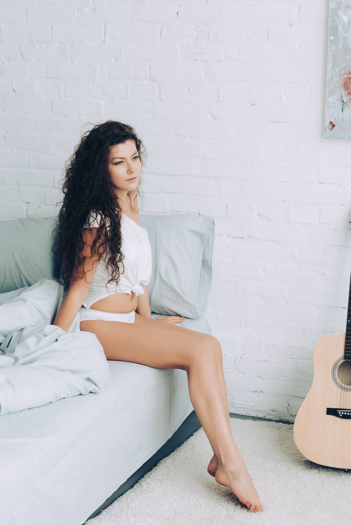 young curly woman sitting on bed during morning time at home - Photo, Image