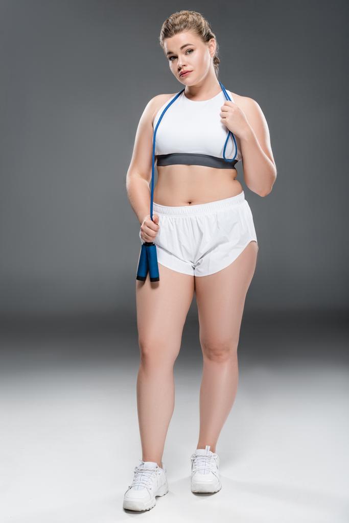 young oversize woman holding jumping rope and looking at camera on grey - Photo, Image