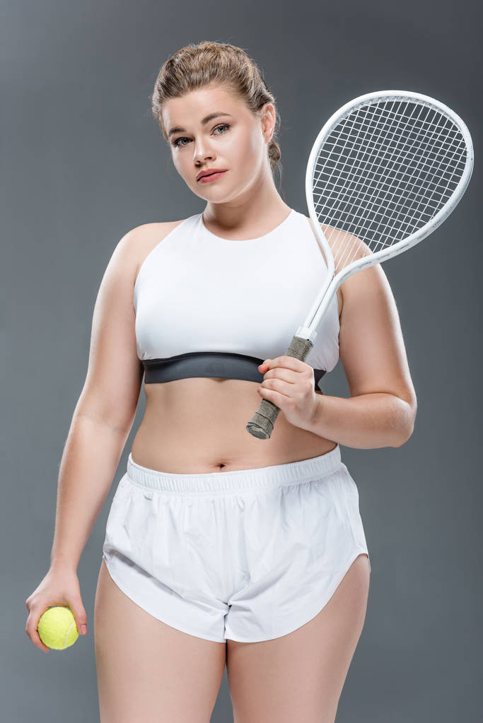 привлекательная толстая женщина, держащая теннисный ракетный мяч изолированный на сером
 - Фото, изображение