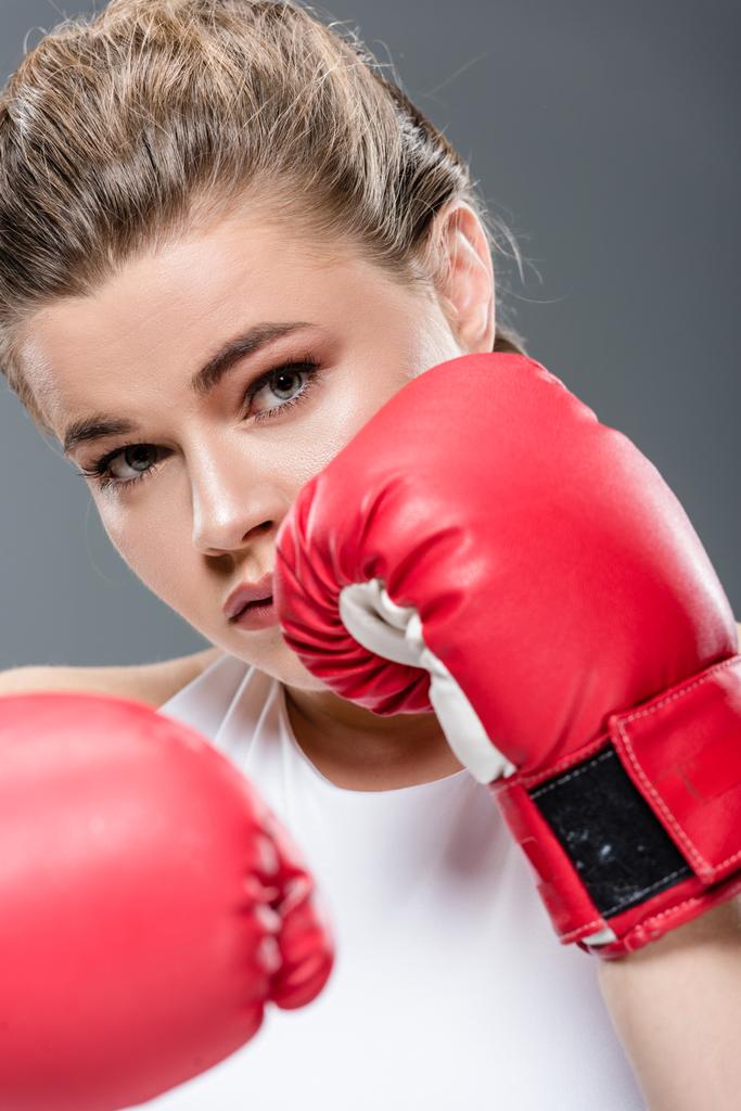 крупным планом молодой женщины в боксёрских перчатках, смотрящей в камеру, изолированную на сером
  - Фото, изображение