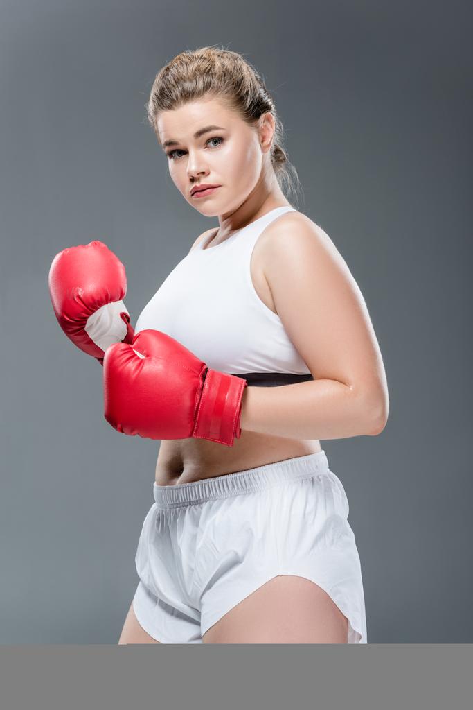 jeune taille plus femme en vêtements de sport et gants de boxe regardant la caméra isolée sur gris
  - Photo, image