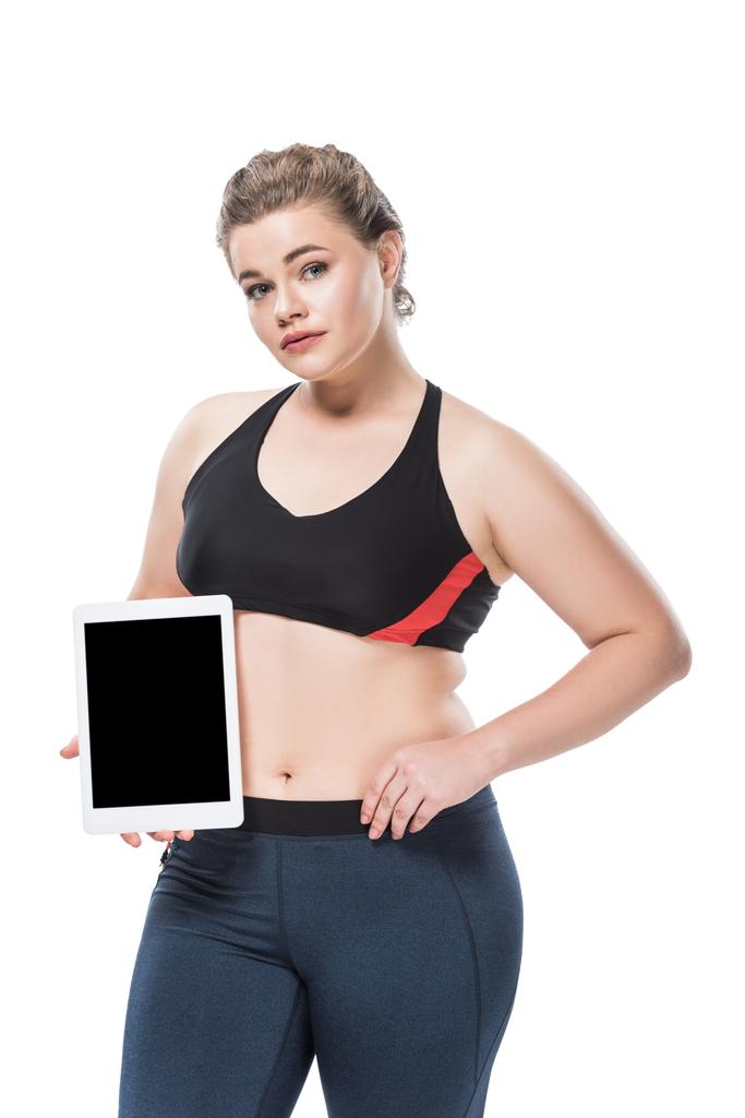 スポーツウェア空白の画面とデジタル タブレットを押しながら白で隔離カメラ目線で若い肥満女性  - 写真・画像