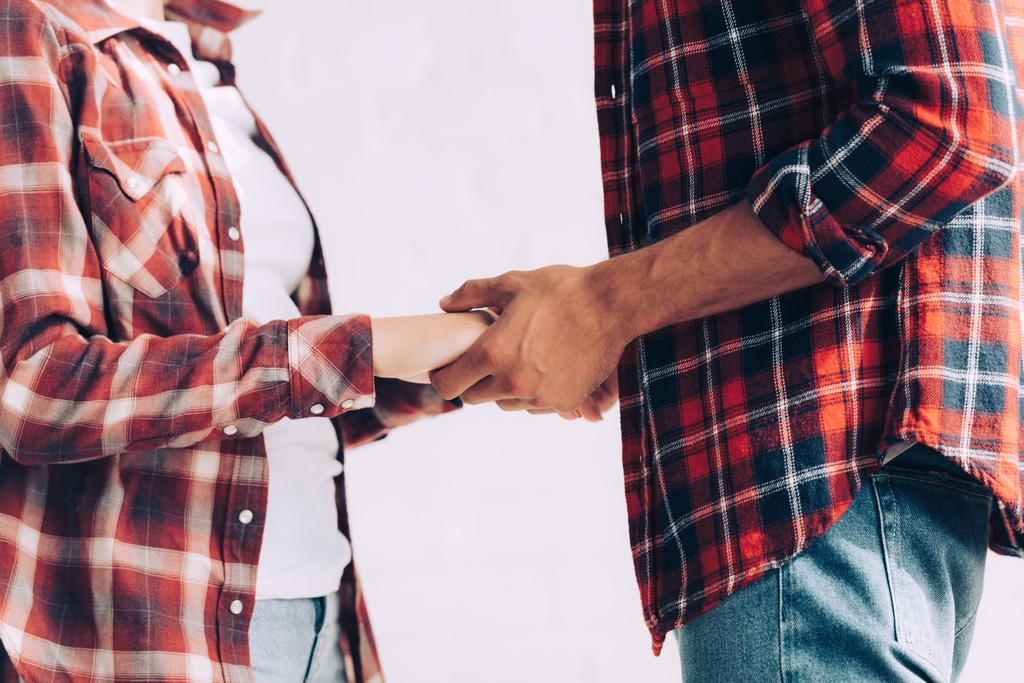 обрезанное изображение пары в клетчатых рубашках, держащихся за руки дома
 - Фото, изображение