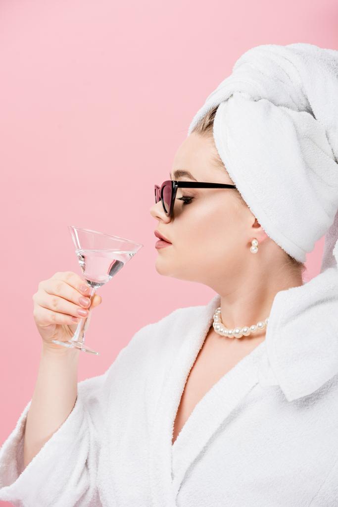 giovane donna oversize in accappatoio, occhiali da sole e asciugamano sulla testa bere da vetro isolato su rosa
    - Foto, immagini