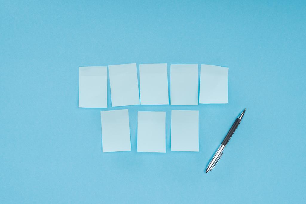 ocho notas adhesivas en blanco con pluma aislada sobre fondo azul
 - Foto, imagen
