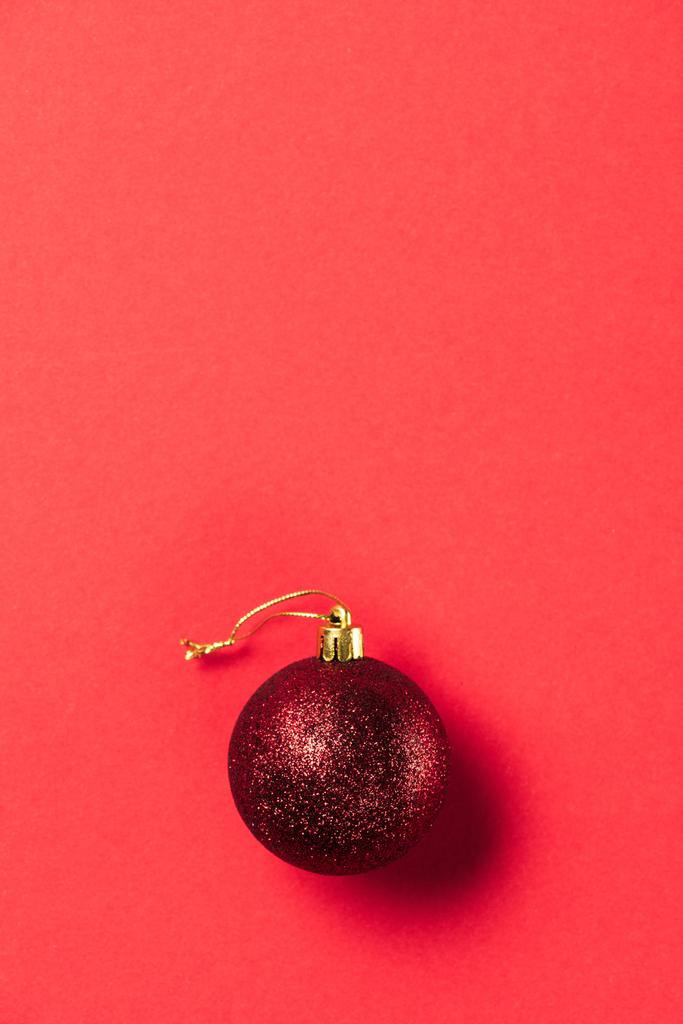 Draufsicht auf rot glänzende dekorative Weihnachtskugel auf rotem Hintergrund - Foto, Bild