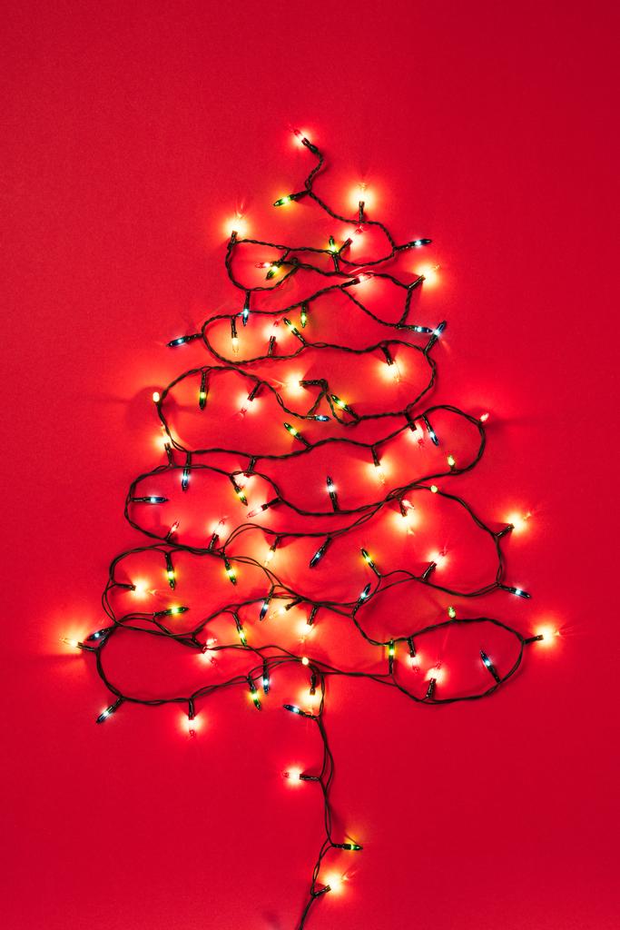 Πολύχρωμες γιρλάντες με τη μορφή του Χριστουγεννιάτικου δέντρου σε κόκκινο φόντο  - Φωτογραφία, εικόνα