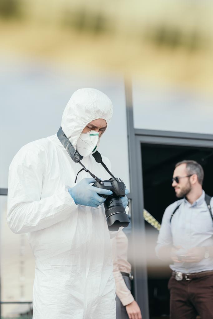 férfi kriminológus védőöltözet és látszó-on fényképezőgép képernyő latex kesztyű - Fotó, kép