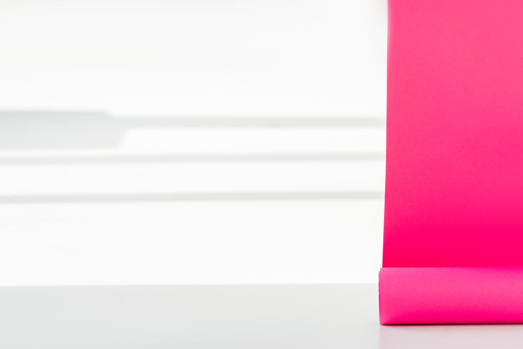 Close up van helder roze papier ophangingen uitgerold op de witte muur met schaduwen - Foto, afbeelding