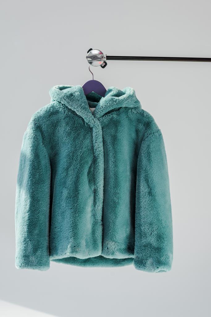 κοντινό πλάνο αφράτο πράσινο faux γούνα παλτό κρέμεται στο ράφι στο γκρι φόντο - Φωτογραφία, εικόνα