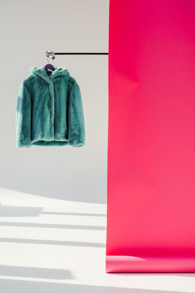 manteau en fausse fourrure vert moelleux sur cintre avec papier peint rose
  - Photo, image