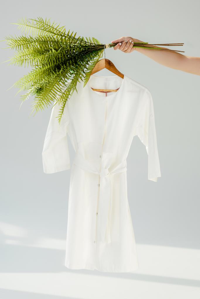 female hand holding hanger with white dress and green plants - Photo, Image