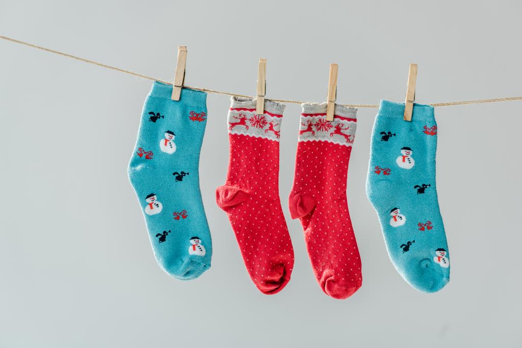 крупным планом разноцветных праздничных зимних носков, висящих на веревке с прищепками, изолированными на сером
 - Фото, изображение