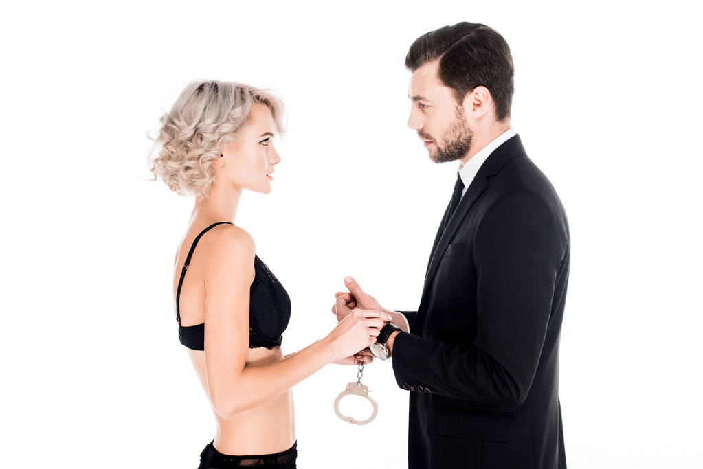 Couple of young adults holding handcuffs and looking at each other isolated on white - Photo, Image