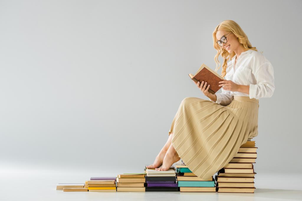 attraente donna a piedi nudi sorridente in occhiali seduto su gradini fatti di libri
   - Foto, immagini