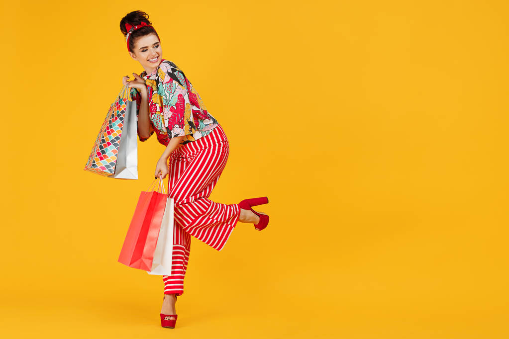 volle Länge Foto von jungen glücklichen kaukasischen Frau in lässigen bunten Kleidern halten Taschen und Einkaufen über orangefarbenem Hintergrund. - Foto, Bild