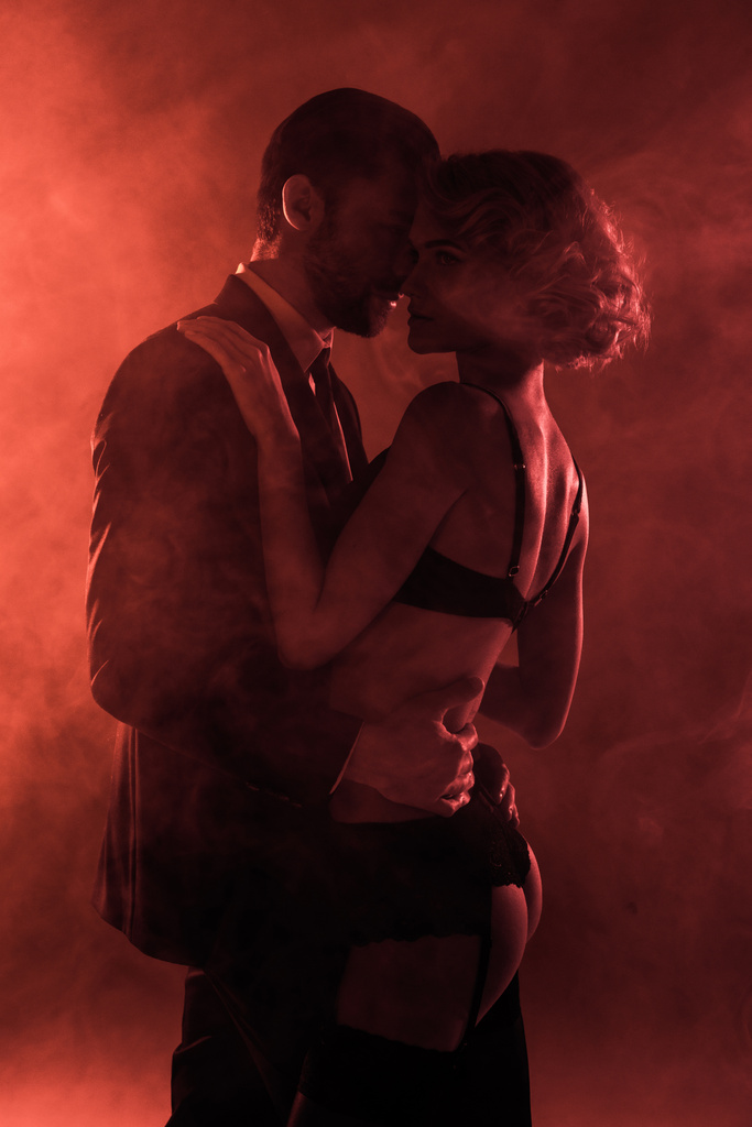 Casal maravilhoso abraçando no fundo de fumaça vermelha
 - Foto, Imagem