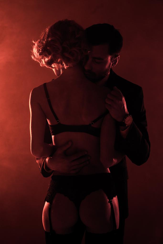 Uomo che abbraccia l'uomo seducente in lingerie meravigliosa su sfondo fumo rosso
 - Foto, immagini