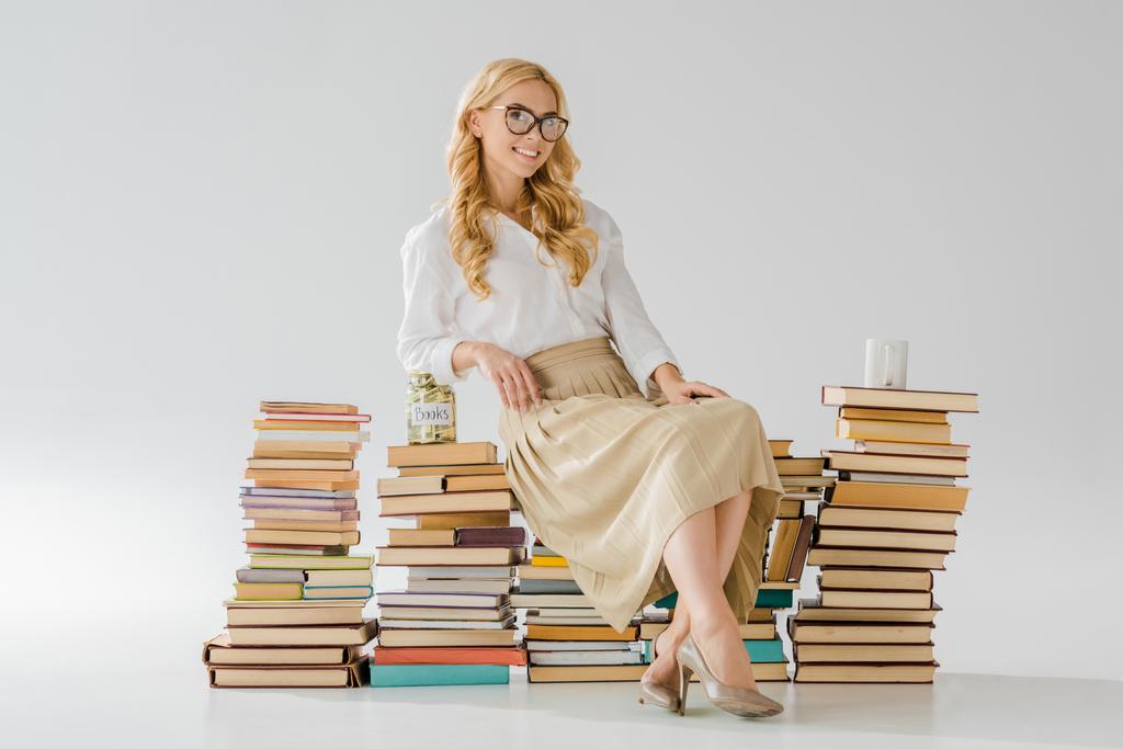 hermosa mujer en gafas sentado en libros con ahorros en frasco y taza
 - Foto, imagen