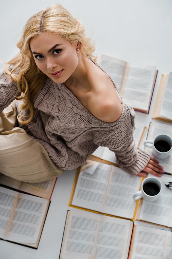 close up of woman sitting on open books with coffee cups isolated on grey - Photo, Image