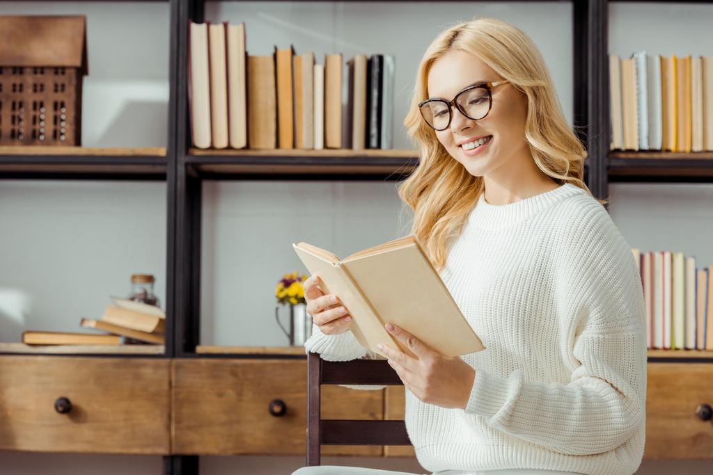 primo piano di bella donna in occhiali seduta e lettura libro in soggiorno
 - Foto, immagini