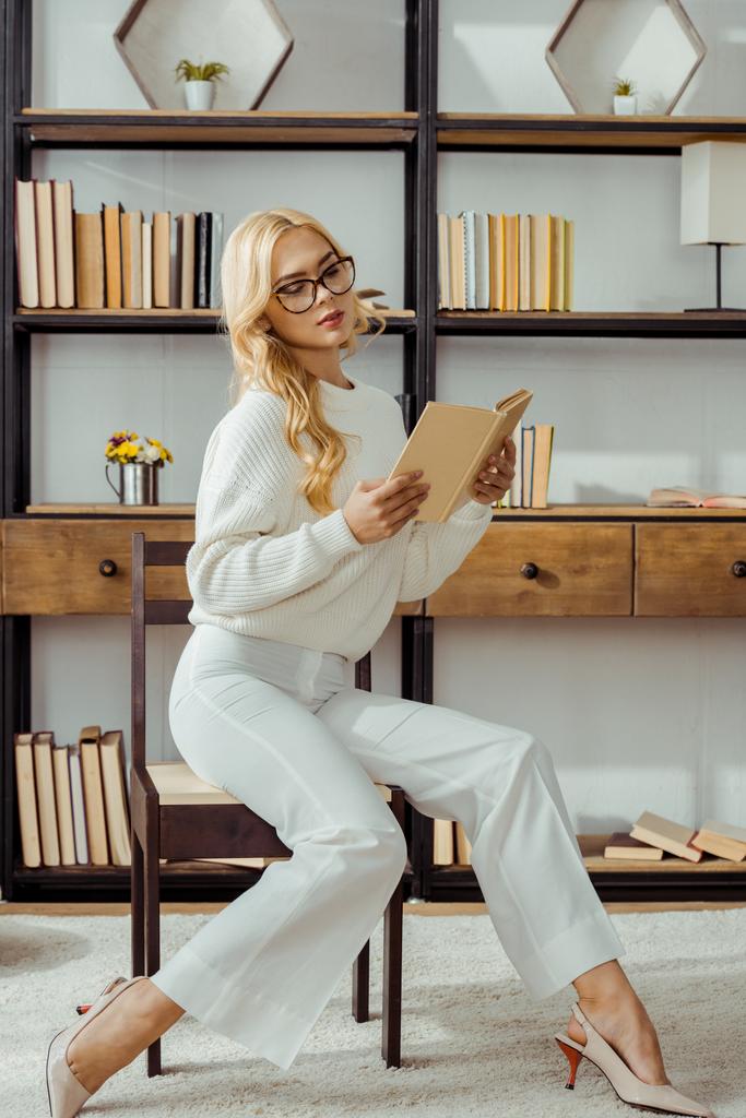 gyönyörű nő szemüveg könyvtárban ül, és könyvet olvas - Fotó, kép