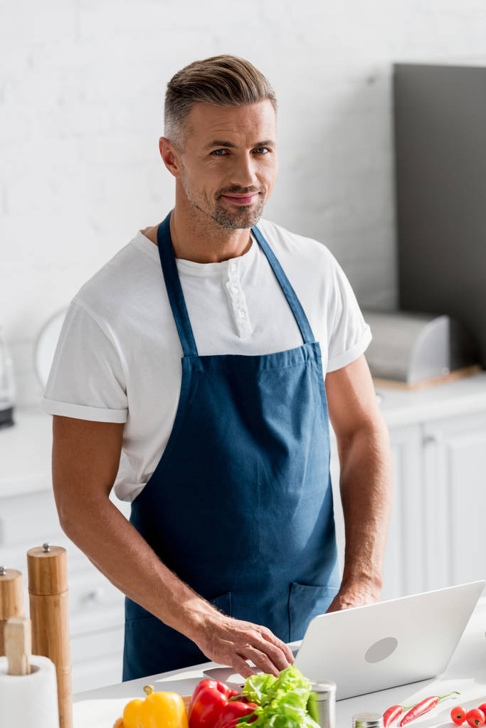 красивий чоловік стоїть на кухні і працює на ноутбуці
  - Фото, зображення