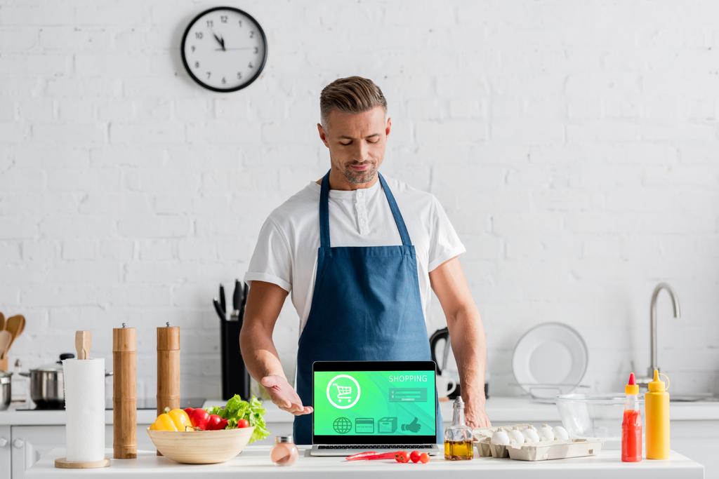 adult man with open laptop and online shopping illustration on screen standing at kitchen - Photo, Image