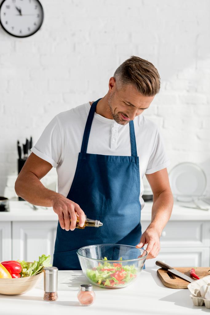 homem adulto adicionando óleo na salada na cozinha
 - Foto, Imagem
