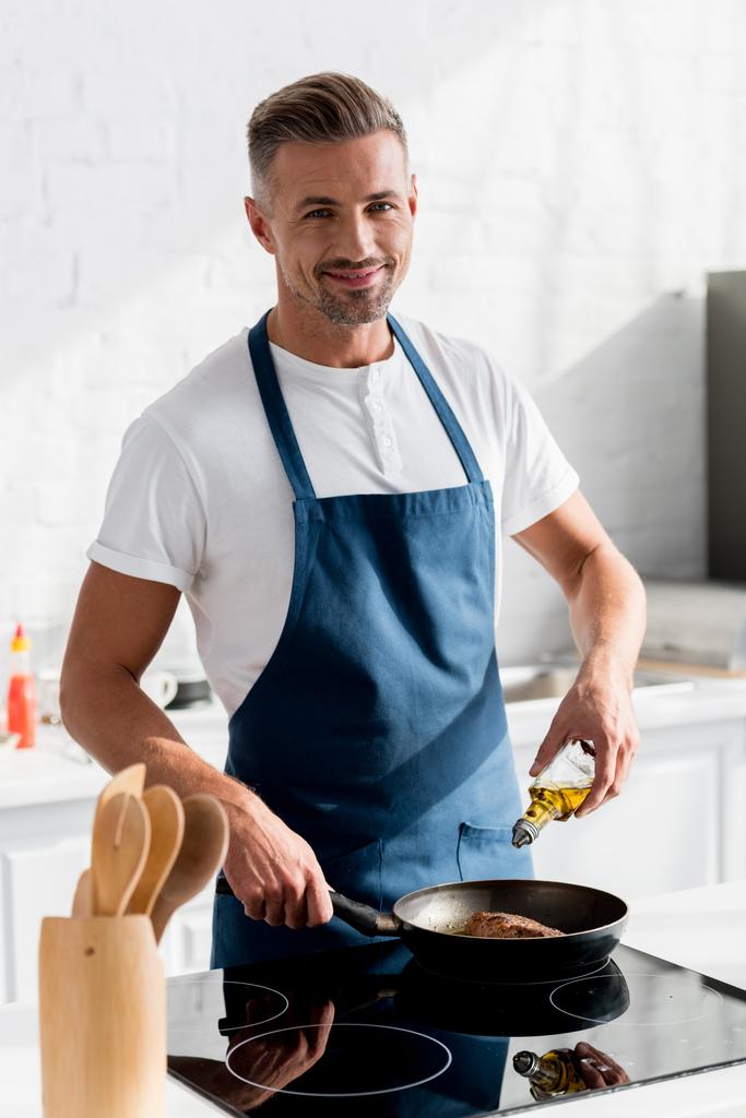 dospělí s úsměvem muž přilévat olej steak v kuchyni - Fotografie, Obrázek