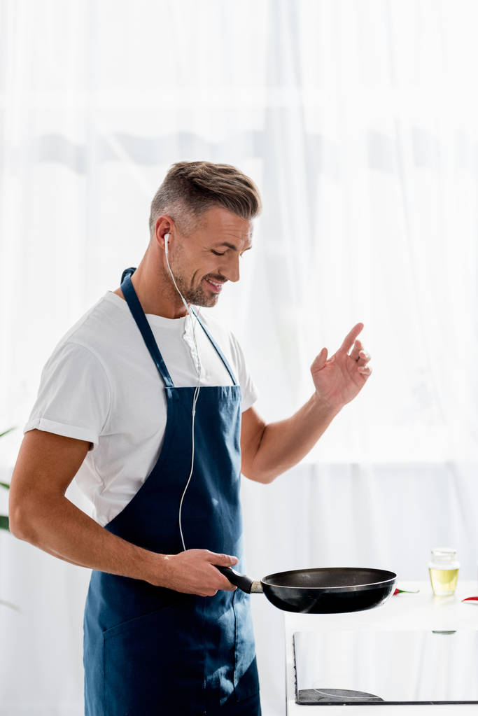 hymyilevä mies, jolla on kuulokkeet ja pannu kädessä kuunnellen musiikkia keittiössä
 - Valokuva, kuva