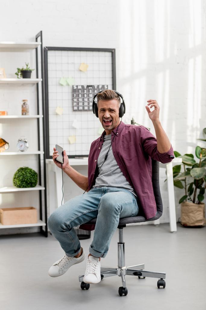 man muziek luisteren en zingen luid zittend op de stoel thuis kantoor - Foto, afbeelding