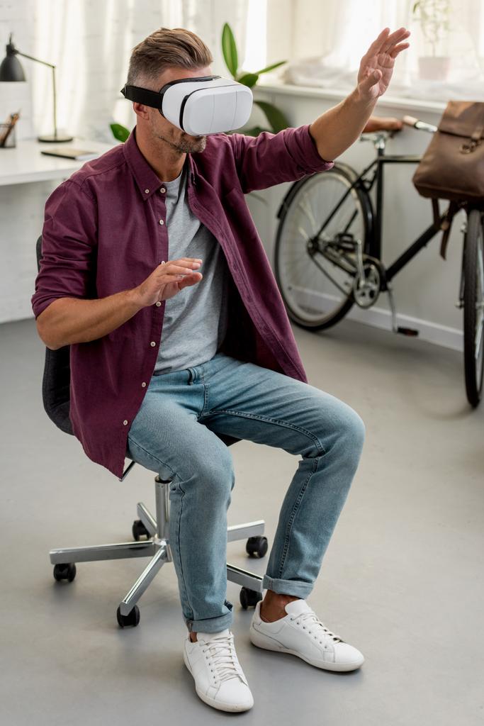 человек сидит на стуле и жестикулирует в гарнитуре виртуальной реальности в домашнем офисе
 - Фото, изображение