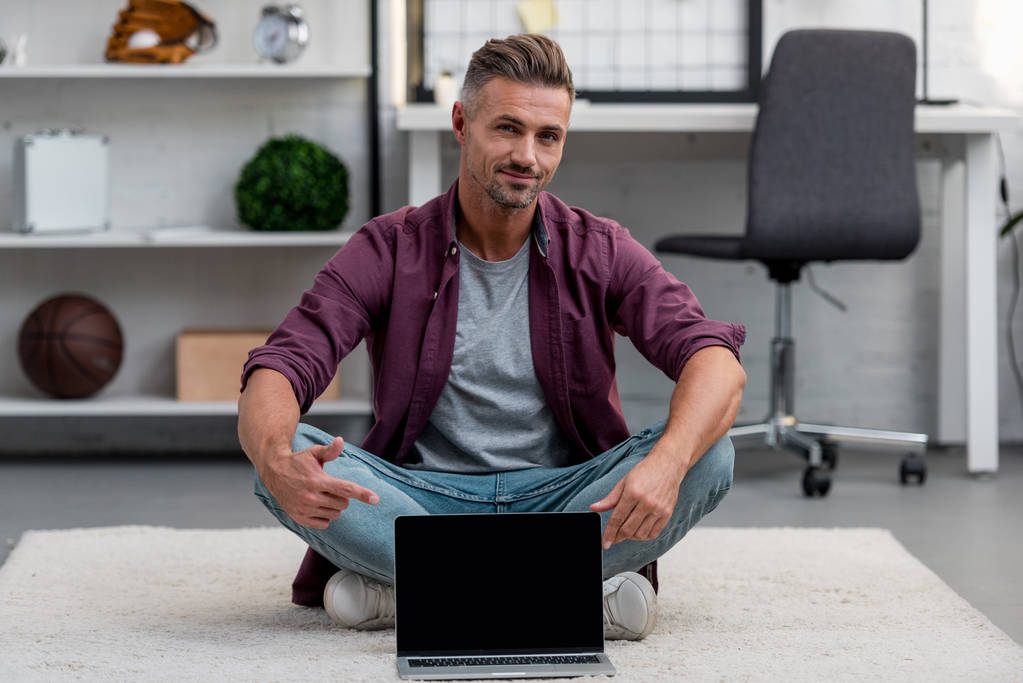 homem bonito sentado em casa escritório com laptop e apontando para a tela em branco
 - Foto, Imagem