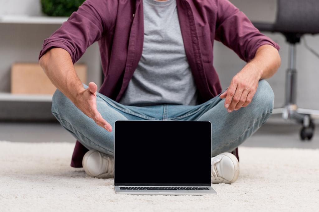 обрезанный вид человека, сидящего с ноутбуком на ковре
 - Фото, изображение