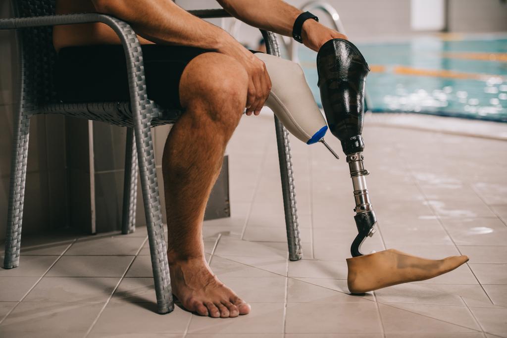 colpo ritagliato di sportivo con gamba artificiale seduto sulla sedia in piscina coperta
 - Foto, immagini
