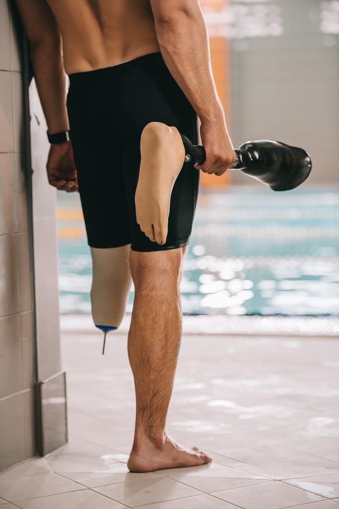 屋内プールのプールサイドに立って押し続ける彼の義足のスポーツマンのクロップ撮影 - 写真・画像