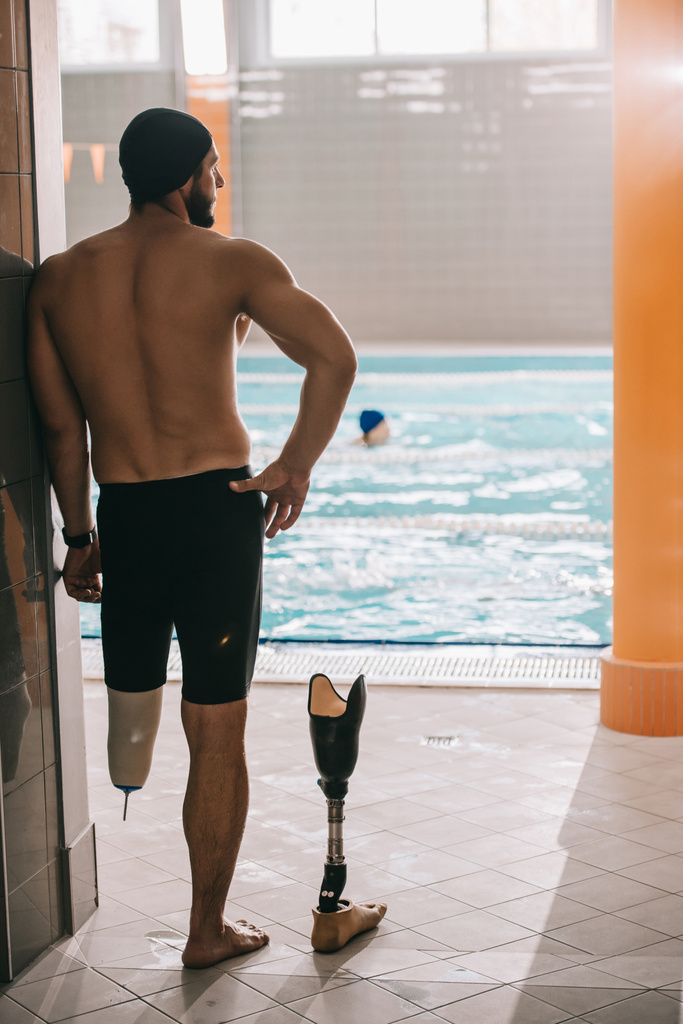 vista trasera del nadador parado junto a la piscina de la piscina cubierta y despegando pierna artificial
 - Foto, imagen