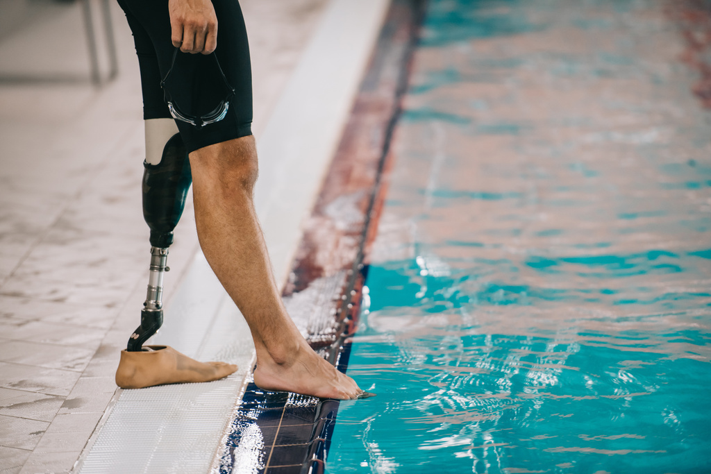 bijgesneden schot van fit zwemmer met kunstmatige been staande op zwembad op overdekt zwembad en de temperatuur van het water van de controle - Foto, afbeelding