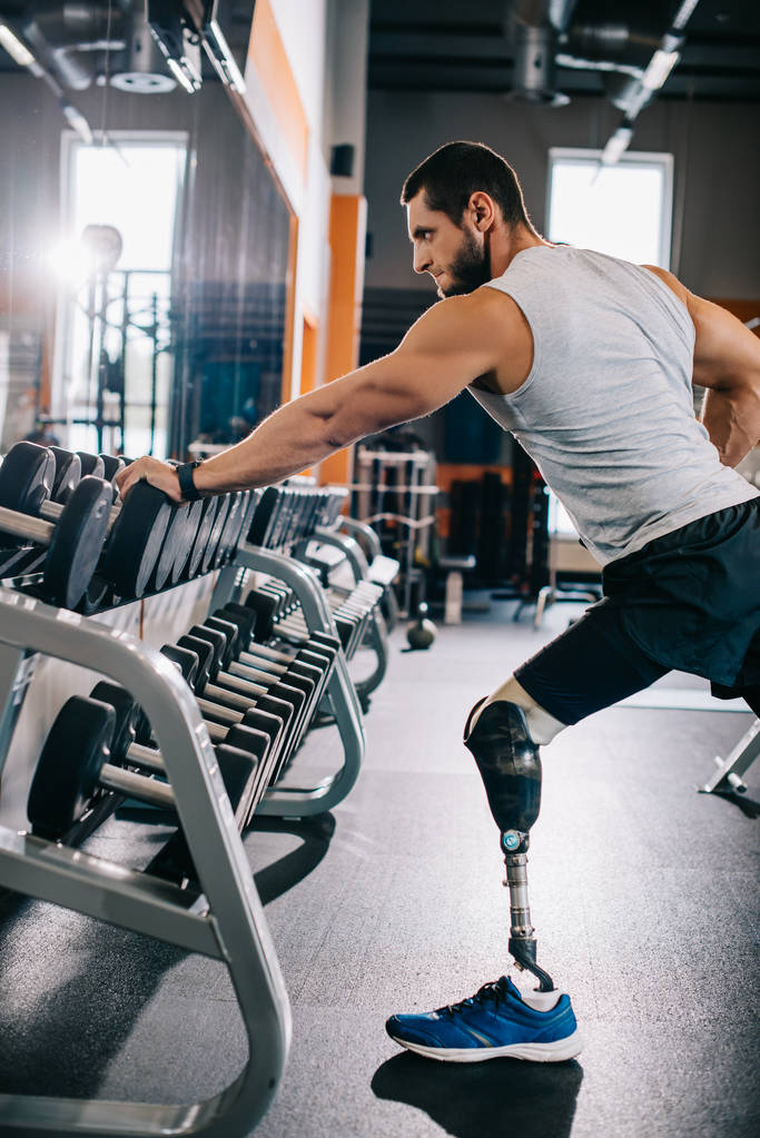 visão lateral do jovem desportista com perna artificial trabalhando com halteres no ginásio
 - Foto, Imagem