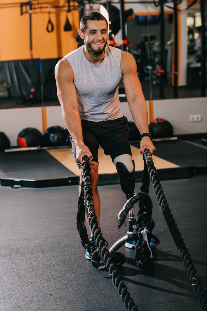 muscular young sportsman with artificial leg working out with ropes at gym - Photo, Image