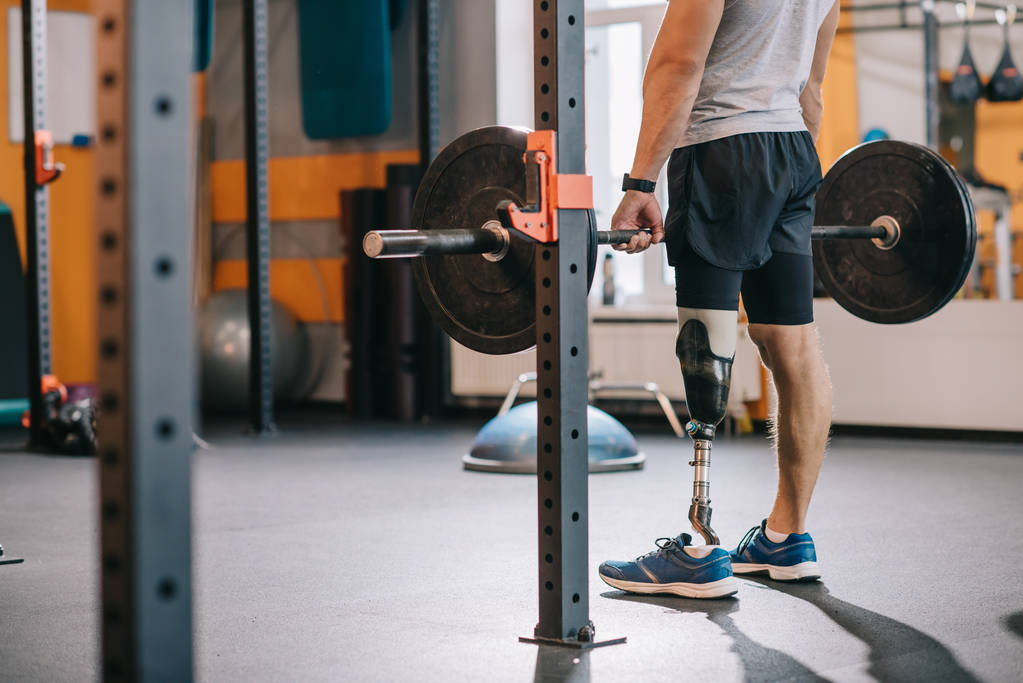 Schnappschuss eines athletischen Sportlers mit Beinprothese beim Training mit der Langhantel im Fitnessstudio - Foto, Bild