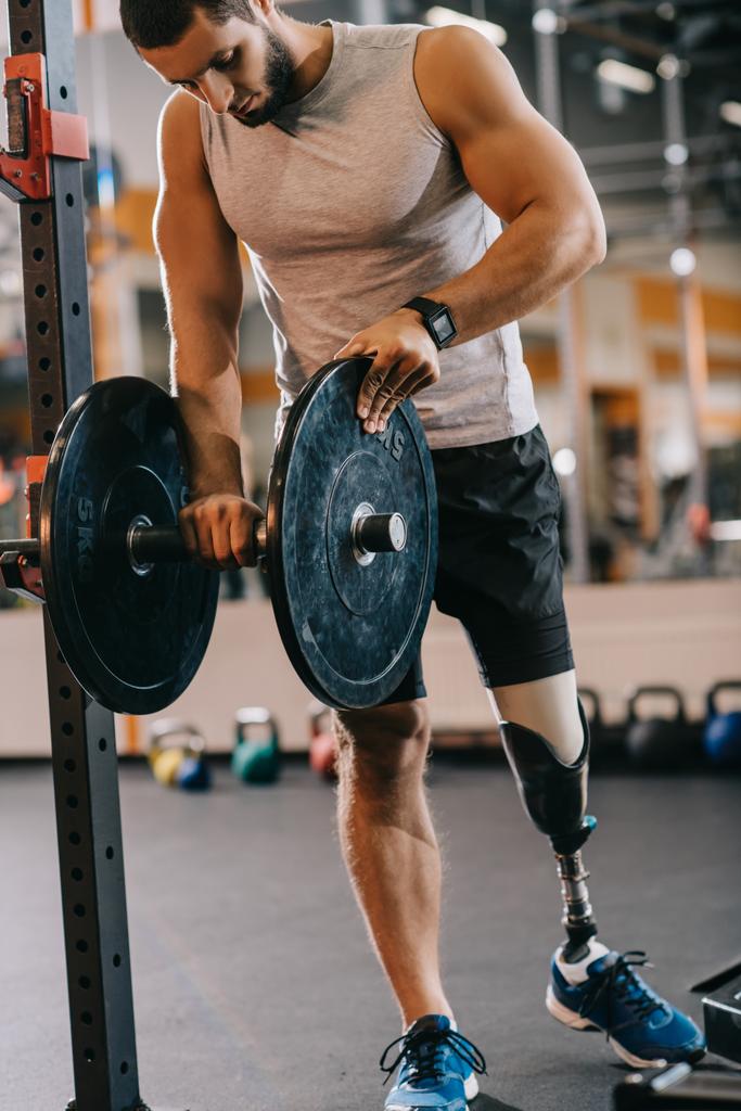 beau jeune sportif avec jambe artificielle se préparant pour l'entraînement avec haltère à la salle de gym
 - Photo, image