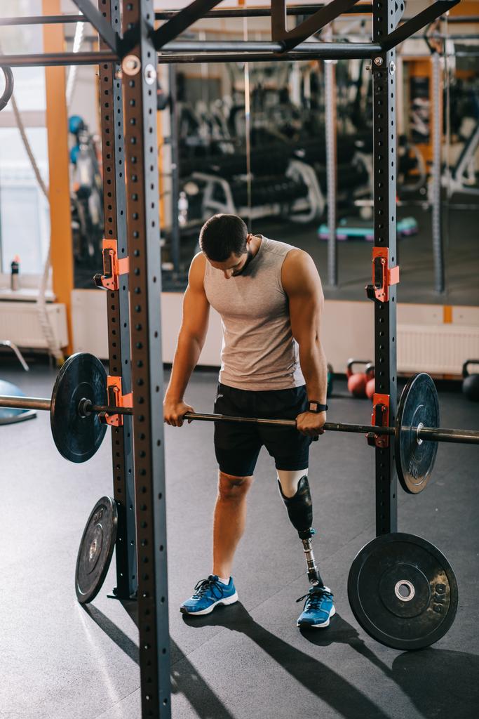 athletic young sportsman with artificial leg working out with barbell at gym - Photo, Image