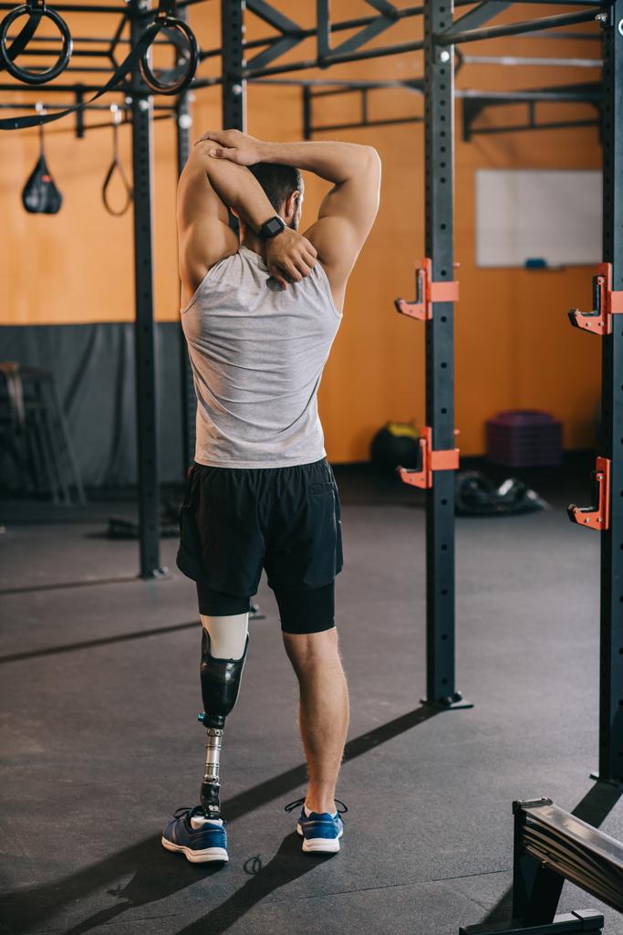 Achteraanzicht van de jonge sporter met kunstmatige been uitrekkende in de buurt van Turnen ladder op sportschool - Foto, afbeelding