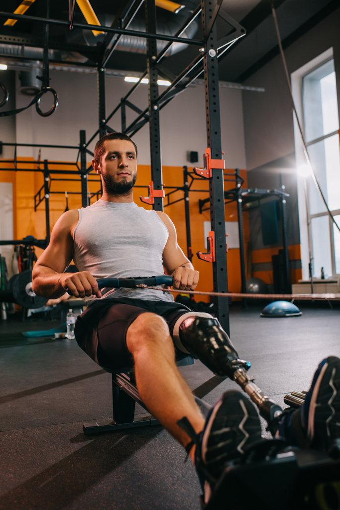 atlético jovem desportista com perna artificial trabalhando com máquina de remo no ginásio
 - Foto, Imagem