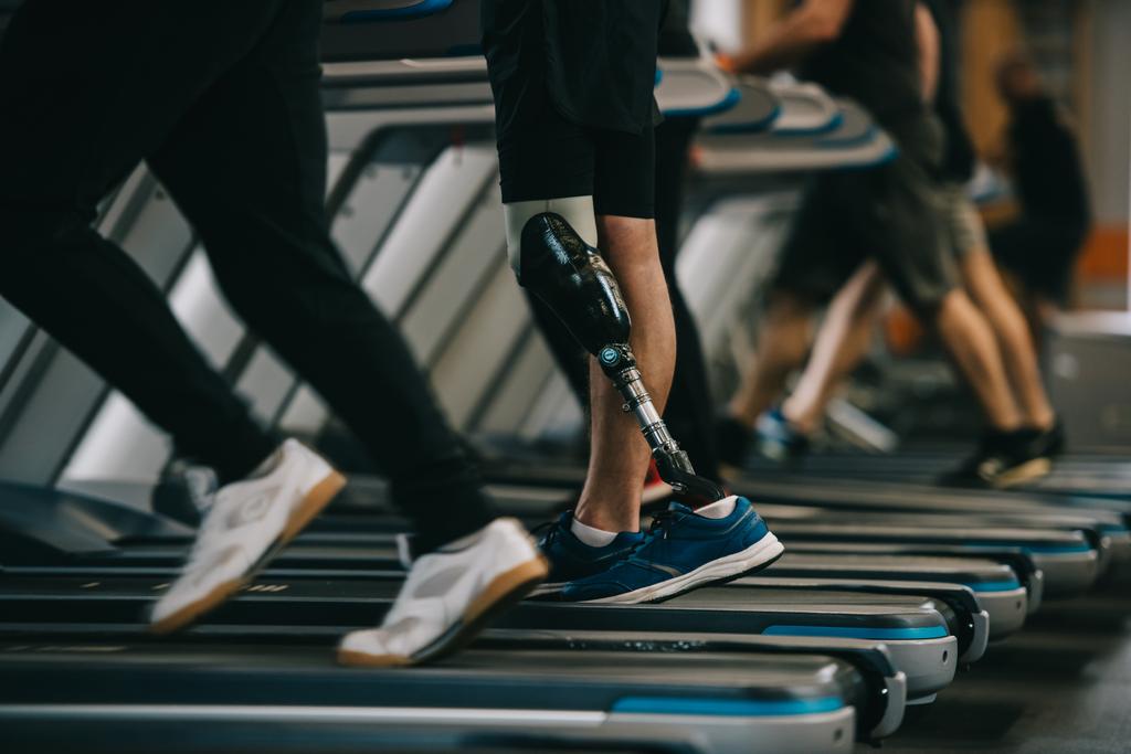 diğer insanlarla spor salonunda koşu bandı üzerinde çalışan yapay bacak ile sporcu kadeh kırpılmış - Fotoğraf, Görsel