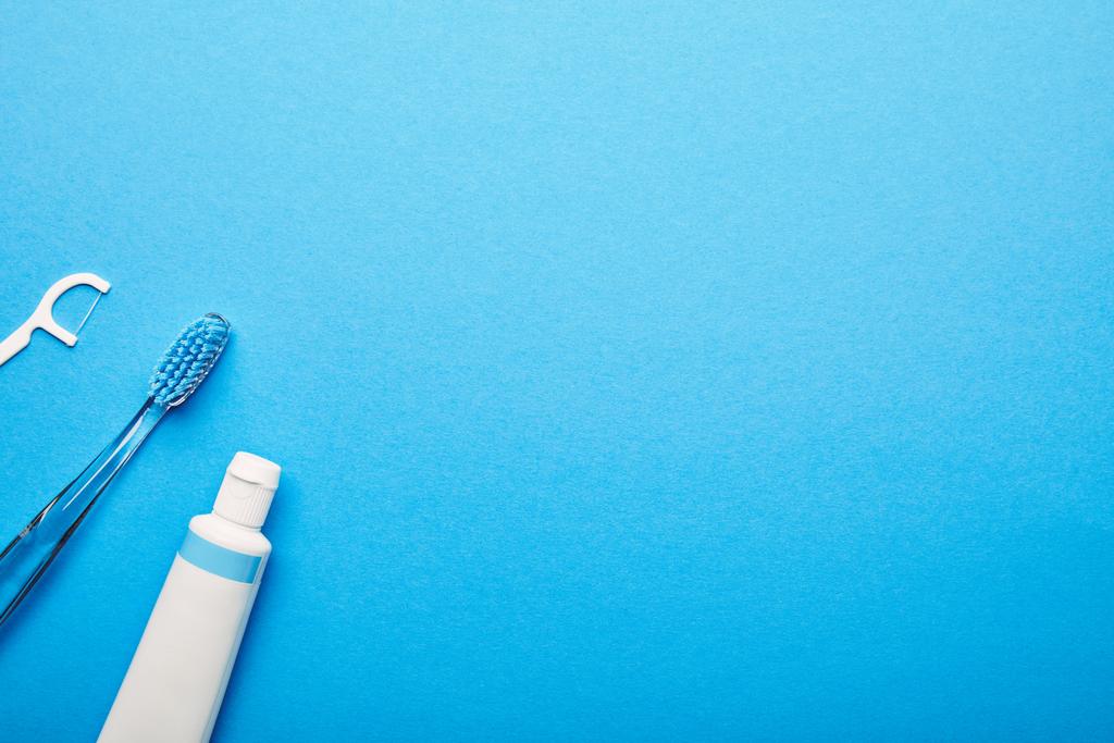 Zahnseide, Zahnbürste und Zahnpasta auf blauem Hintergrund, Zahnheilkonzept - Foto, Bild