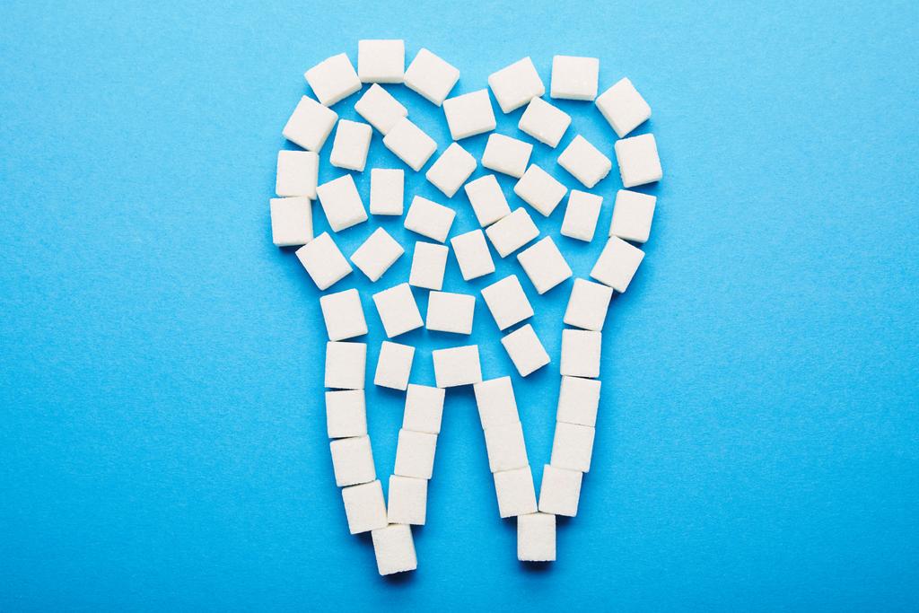vista superior de los cubos de azúcar blanco dispuestos en el signo dental sobre fondo azul, concepto de cuidado dental
 - Foto, Imagen